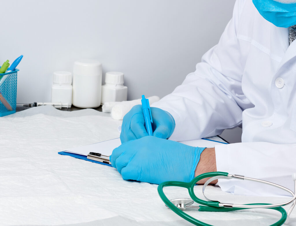 Un médico con una bata blanca se sienta en una mesa y escribe con un